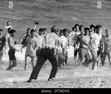 Students riot during Spring Break at Ft. Lauderdale Beach.  Ca. 1960's.. Here taunting a police officer as he chases them into the surf. Stock Photo