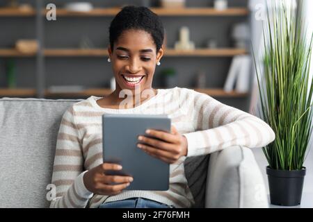 Smiling African American Woman Relaxing On Sofa With Digital Tablet At Home Stock Photo