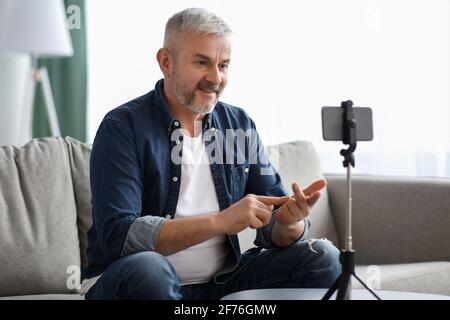 Cheerful matured man broadcasting from home, using smartphone Stock Photo