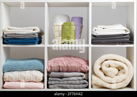 Stacks of towels, sheets, bedding, clothes, blanket and pillow on a white shelf. Stock Photo
