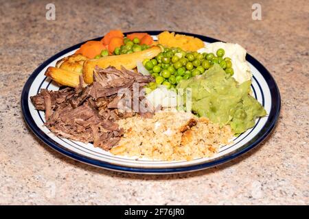 Sunday dinner of slow cooked shredded pulled beef on a plate with plenty of vegetables such as peas, mushy peas, parsnips, roast potatoes and carrots, Stock Photo
