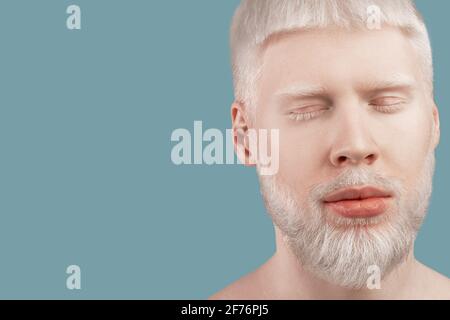 Bearded albino man posing with closed eyes against turquoise studio background, empty space. Albinism concept Stock Photo