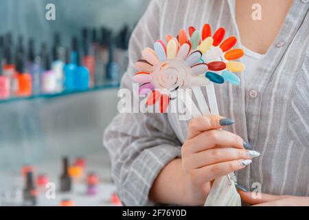 Female hands with artificial acrylic nails picks up new polish color for manicure design. Assortment of nail polishes for coloring nail in beauty salo Stock Photo