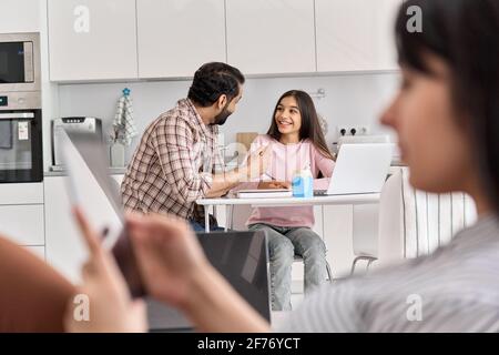 Indian husband helping teen daughter with studies while wife relaxing at home. Stock Photo