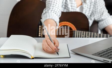 Online musical guitar e education. Online training lesson classes playing guitar at home. Musician practicing acoustic guitar via laptop. Woman writin Stock Photo