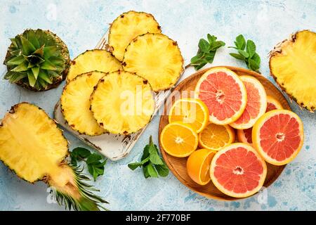 Sliced ripe pineapple, orange and grapefruit on light blue stone background. Tropical fruits. Top view. Free space for text. Mock up. Stock Photo