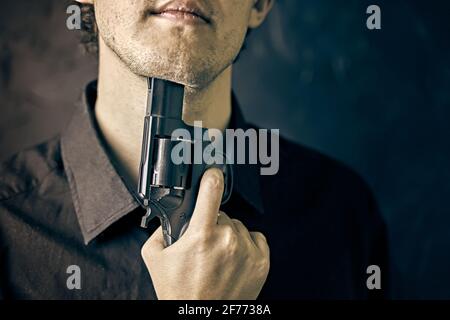 Man with gun is preparing to commit suicide. Depression with fatal outcome. Young man put muzzle of gun to his chin. Stock Photo
