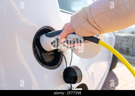 Close up woman hand inserts power cable supply to charge electric or EV car. Stock Photo