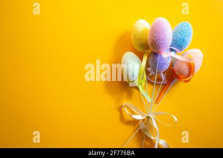 Bouquet of fluffy colorful plastic eggs isolated on yellow background. Easter concept. Stock Photo