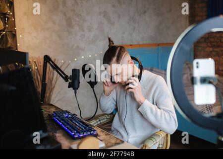 Man recording video on smartphone during the work at home on computer. Young guy recording on professional microphone speash about music Stock Photo