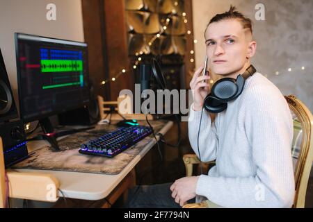 Young man call to friend in order for him listen music that he record. Self isolated man at home during quarantine working on computer and use phone Stock Photo