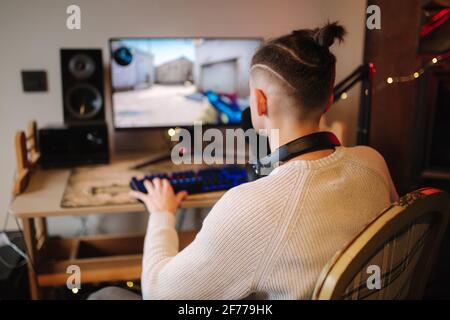 Men playing online video games at home using powerful computer. Streamer man using professional microphone, keypad, mouse in gaming home studio. Back Stock Photo