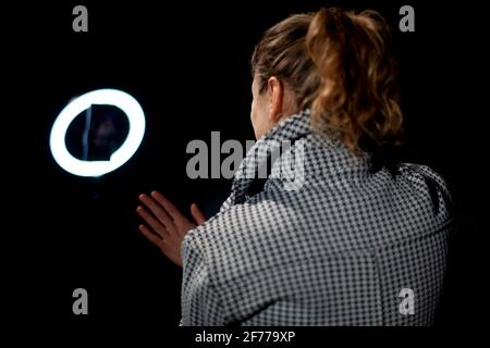 The girl removes the blog. The girl uses a round lamp to illuminate her face. Shooting a video blog with artificial light. A woman in a jacket and wit Stock Photo