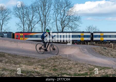 Mountain and BMX bike track at Edenbrook Country Park with cyclist riding, and a train in the background, Fleet, Hampshire, UK Stock Photo