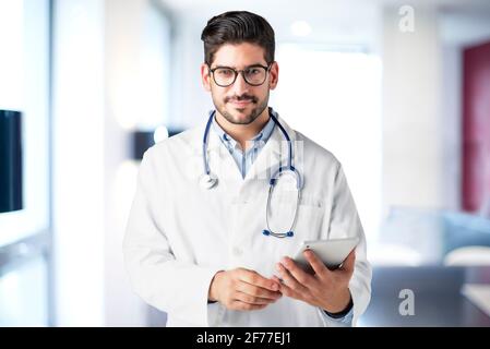 Shot of male doctor holding digital tablet in his hand while standing in hospital’s foyer. Stock Photo