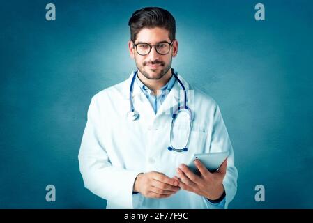 Portrait shot of male doctor holding digital tablet in his hand while standing at isolated background. Copy space. Stock Photo