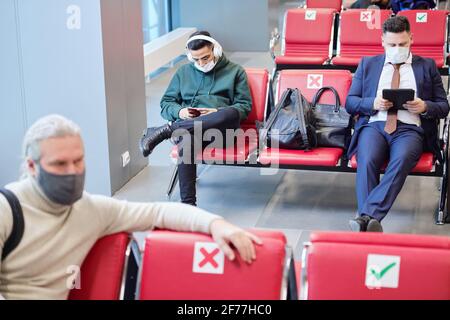 Young man with headphones listening to music and scrolling in smartphone while businessman using digital tablet in lounge Stock Photo
