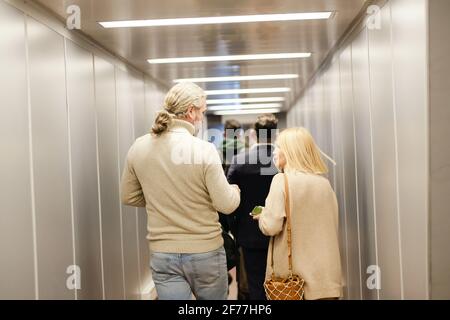 Back view of mature couple in casualwear, business traveler and young man with baggage moving forwards along corridor in airport Stock Photo