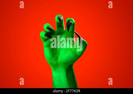 Halloween, nightmare creature and evil monster horror story concept with a scary zombie or demon hand with creepy long black nails isolated on orange Stock Photo
