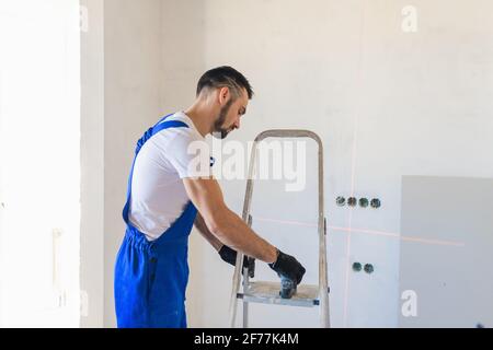 A man in overalls marks the wall using a laser level Stock Photo