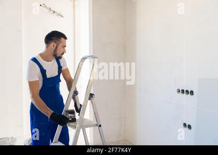 A adjuster in overalls marks the wall using a laser level Stock Photo