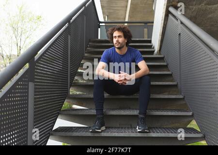 a male athlete rests seated on a staircase during a training session Stock Photo