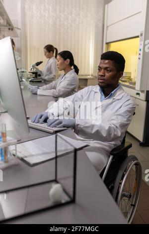 African scientist sitting in wheelchair and typing on computer while working in the laboratory Stock Photo