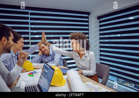 Multicultural group of architect sitting in office and having meeting about new project. Mixed race woman giving high five to her colleague. Stock Photo