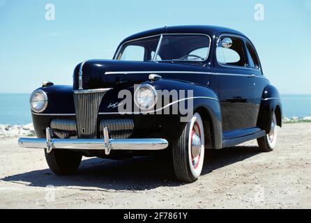 1940s 1941 FORD COUPE V8 SUPER DELUXE AUTOMOBILE NAVY BLUE PAINT WHITEWALL TIRES PARKED NEAR OCEAN SEASHORE BEACH - 002230 LAH001 HARS OLD FASHIONED Stock Photo