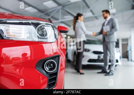 Close up of headlights of a car. In blurry background are car seller and customer shaking hands. Stock Photo