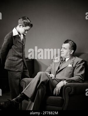 1940s MAN FATHER SEATED TALKING TO DISCIPLINING ADMONISHING PRE-TEEN BOY SON STANDING WITH HEAD BOWED ASHAMED - j4426 HAR001 HARS FACIAL ANGER COMMUNICATION STRONG SONS CONTROL FAMILIES LIFESTYLE PARENTING STUDIO SHOT HOME LIFE SEATED COPY SPACE FRIENDSHIP HALF-LENGTH PERSONS DISCIPLINE CARING MALES TEENAGE BOY EXPRESSIONS FATHERS B&W LECTURE HIGH ANGLE HIS SORRY DADS AUTHORITY DISCIPLINED RULES ASHAMED CONCEPTUAL TEENAGED OBEY PERSONAL ATTACHMENT AFFECTION BEHAVIOR BOWED EMOTION JUVENILES MID-ADULT MID-ADULT MAN OBEDIENCE PARENTAL PRE-TEEN PRE-TEEN BOY SCOLD TOGETHERNESS BLACK AND WHITE Stock Photo