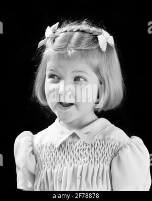 1940s SMILING CUTE BLOND GIRL LOOKING OFF TO SIDE WITH MISCHIEF IN EYES BOWS AND BRAID IN HAIR AND SMOCKING ON DRESS  - j9183 HAR001 HARS COMIC SWEET PLEASED JOY LIFESTYLE SATISFACTION FEMALES WINNING STUDIO SHOT HEALTHINESS HOME LIFE COPY SPACE HALF-LENGTH EXPRESSIONS B&W HUMOROUS HAPPINESS CHEERFUL MISCHIEF AND EXCITEMENT COMICAL IN ON TO SMILES BOWS COMEDY JOYFUL STYLISH PLEASANT AGREEABLE BRAID CHARMING JUVENILES LOVABLE PERSONABLE PLEASING ADORABLE APPEALING BLACK AND WHITE CAUCASIAN ETHNICITY HAR001 LOOKING TO SIDE OLD FASHIONED SMOCKING Stock Photo