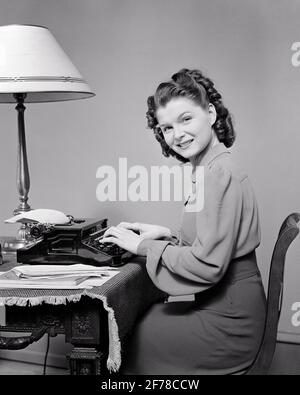 1940s WOMAN SEATED AT HOME DESK USING PORTABLE TYPEWRITER HEAD TURNED LOOKING AT CAMERA SMILING - s7435 HAR001 HARS CAREER YOUNG ADULT INFORMATION PLEASED JOY LIFESTYLE FEMALES JOBS HOME LIFE SEATED COPY SPACE HALF-LENGTH LADIES PERSONS INSPIRATION PROFESSION CONFIDENCE PORTABLE B&W EYE CONTACT SKILL OCCUPATION SKILLS HEAD AND SHOULDERS CHEERFUL LEISURE TYPING CAREERS KNOWLEDGE RECREATION LABOR PRIDE EMPLOYMENT OCCUPATIONS SMILES TURNED USING CONCEPTUAL AUTHOR JOYFUL STYLISH WRITER EMPLOYEE CREATIVITY YOUNG ADULT WOMAN BLACK AND WHITE CAUCASIAN ETHNICITY HAR001 LABORING OLD FASHIONED TYPIST Stock Photo