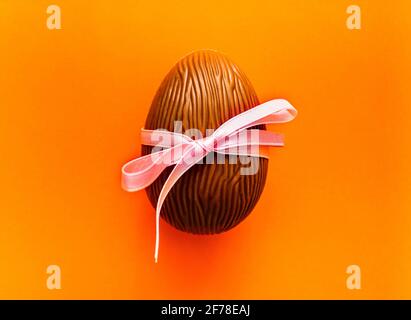 Chocolate Easter egg with pink ribbon on orange background. Spring holidays concept Stock Photo