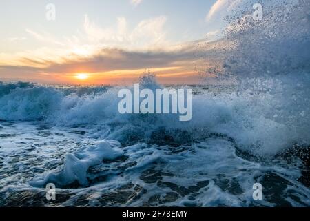 A Sunset Ocean Wave is Breaking on the Sea Shore with the Sun Setting on the Ocean Horizon Stock Photo