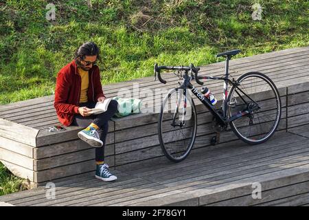 Young man sitting and reading book in a park in spring Stock Photo