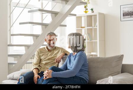 Happy mature older couple laughing and talking sitting at home on couch. Stock Photo