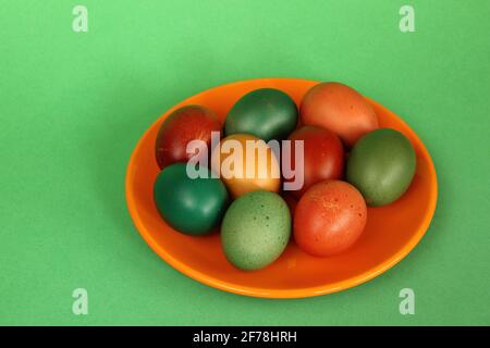Colorful painted easter eggs on orange plate close up on green background Stock Photo
