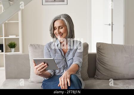 Happy old woman using digital tablet having virtual online meeting at home. Stock Photo