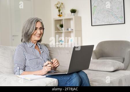 Happy mature mid age woman working on laptop computer from home office. Stock Photo