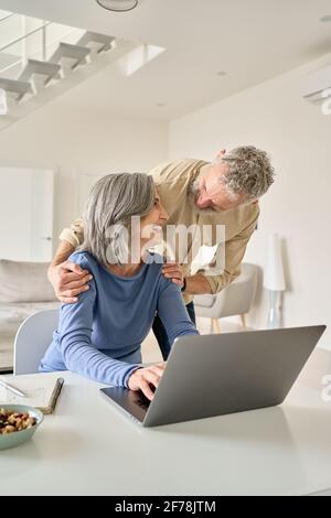Happy mature senior couple laughing using laptop computer at home. Stock Photo