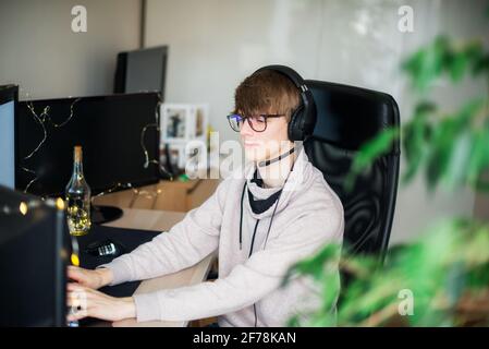 Young gamer playing a video game on pc wearing headphones. Generation Z man chatting, have a video call in his room. Technology in everyday life Stock Photo