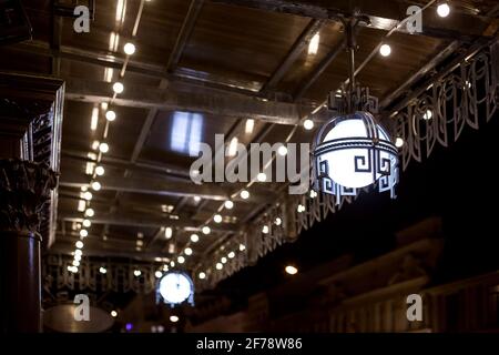 forged iron hanging lanterns under a visor with decorative garlands hanging in a row of lighting in a retro style architecture of the night city. Stock Photo