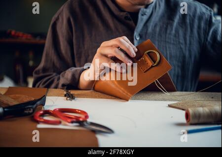 Close-up photo the hands of a skilled shoemaker make a bag from a piece of genuine leather. Stock Photo