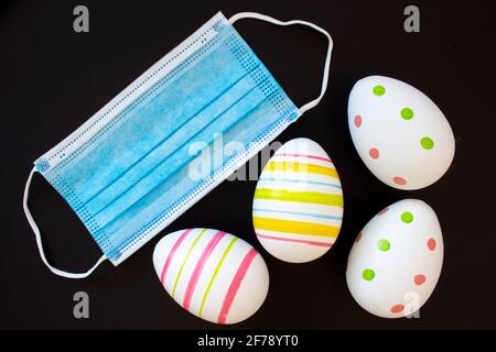 Decorate Easter eggs with a surgical face mask on a black background. Concept: Easter during covid-19 pandemic Stock Photo