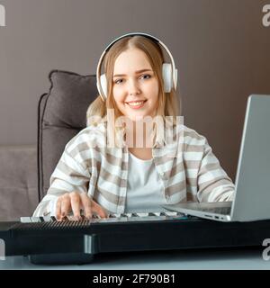 Woman in headphones dj record audio music using laptop.Teenager girl play synthesizer piano during online lesson, learn to play piano online at home i Stock Photo