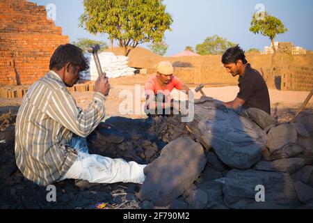 Three men breaking coal in pieces in the brick kiln site Stock Photo