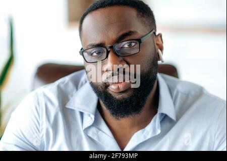Close-up portrait of an attractive confident successful intelligent serious african american bearded man with glasses, wearing a stylish formal shirt, concentrated looking at the camera Stock Photo