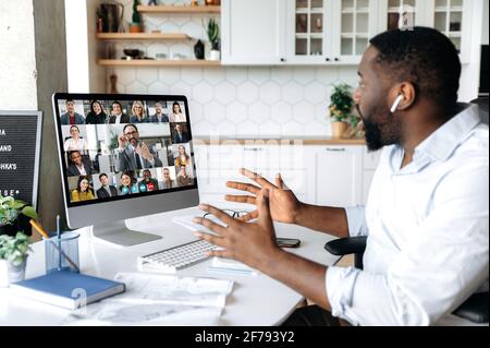 Virtual meeting. Successful African American business man sits at work desk at home, looks at the computer screen, communicates on a video conference with his colleagues, discusses a business plan Stock Photo