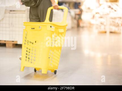 Female hand pulling the yellow plastic trolley for shopping to buy the decoration element for intrior room. Stock Photo